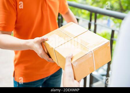 Le liveur est en uniforme orange et porte une boîte à colis à un client - concept de service de messagerie Banque D'Images
