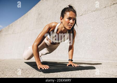 femme de fitness faisant de larges exercices de grimpeurs de montagne. Femme dans les vêtements de sport s'exerçant sur le tapis de fitness à l'extérieur. Banque D'Images