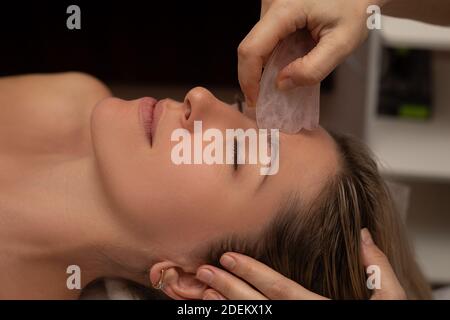 Jeune et belle femme pendant le massage traditionnel chinois - Gua Sha. Gros plan. Soins de beauté dans le salon DE SPA. Outils de beauté dans la main de bea Banque D'Images