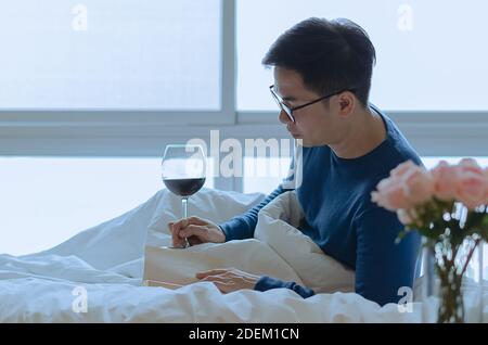 Une personne lisant un livre au lit avec un verre de vin rouge. Concept de détox numérique et de déconnexion sociale. Banque D'Images