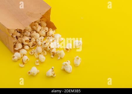 Vue en grand angle du pop-corn qui se déverse de papier brun sac sur fond jaune Banque D'Images