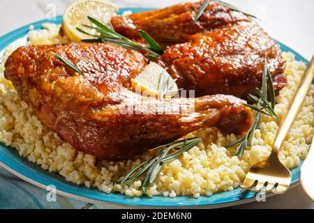 Des quartiers de cuisses de poulet servis sur le millet sur une assiette avec des couverts dorés, des quartiers de citron et des brins de romarin frais sur un fond de pierre en marbre blanc Banque D'Images