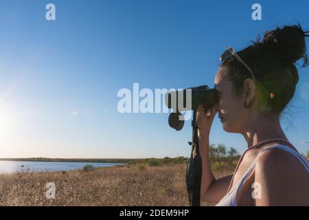 jeune femme regardant avec ses jumelles à l'horizon pendant en vacances dans un lac en été Banque D'Images