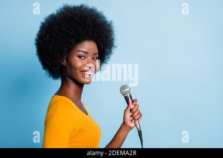 Photo profil de côté portrait de jolie fille à la peau noire tenue microphone souriant isolé sur fond bleu vif Banque D'Images