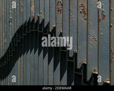 Fragment d'une clôture noire faite de bandes d'acier illuminées par le soleil du côté. Poches de rouille sur métal. Image abstraite. Banque D'Images