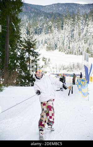 Touriste à la station de ski de levage sur la corde de l'ascenseur de la traînée de ski, essayant de garder l'équilibre. Paysage incroyable dans la vallée en arrière-plan. Concept de sports saisonniers. Banque D'Images