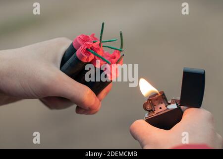 Homme illuminant plusieurs pétards dans sa main en utilisant l'allume-cigare essence. Guy se préparer pour le nouvel an avec des feux d'artifice ou des produits pyrotechniques - gros plan, vue arrière Banque D'Images