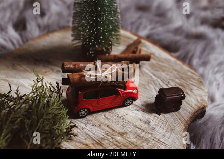 NIS, Serbie - 29 novembre 2020 voiture jouet rouge avec un bouquet de bâtons de cannelle sur le toit et des cubes de chocolat sur une bûche en bois avec arbre de Noël à la maison Banque D'Images