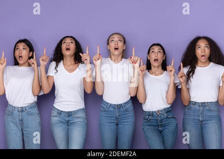 Cinq femmes émerveillement pointant des doigts vers le haut sur fond violet Banque D'Images