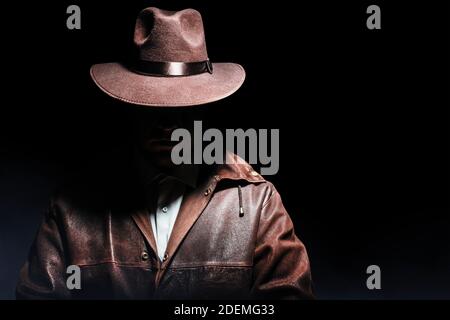Photo d'un détective ombré en veste et chapeau sur fond noir. Banque D'Images