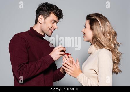 jeune homme décontracté faisant la proposition de mariage à la femme heureuse isolée en gris Banque D'Images