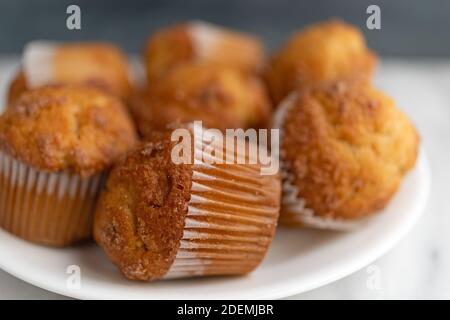 Vue très rapprochée de plusieurs muffins à la banane Streusel sur une plaque blanche au-dessus d'un plan d'examen en marbre avec un mur gris flou en arrière-plan. Banque D'Images