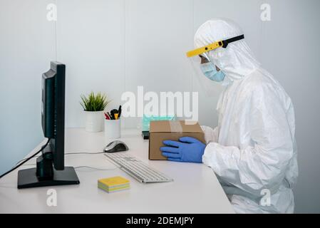 Médecin en costume de protection et en plastique masque facial paquet nouveaux masques médicaux dans une boîte pendant Covid19 à l'hôpital. Homme portant des gants de main et des EPI en int Banque D'Images