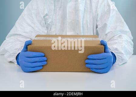 Une infirmière en costume de protection présente une boîte avec les deux mains dans un hôpital. Le travailleur de la santé reçoit des fournitures médicales pour lutter contre le coronavirus Covid 19. Banque D'Images