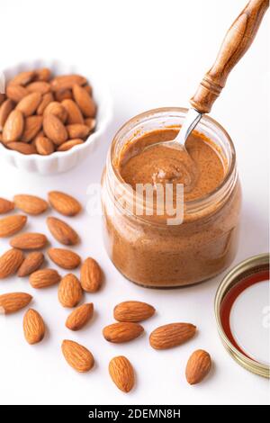 Un petit pot en verre de beurre d'amande avec une cuillère et les amandes crues sur fond blanc Banque D'Images