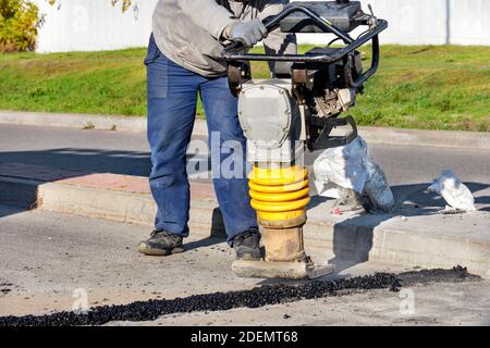 Un travailleur routier utilise un rameur vibrant à essence pour réparer l'asphalte sur la chaussée par une journée ensoleillée. Banque D'Images