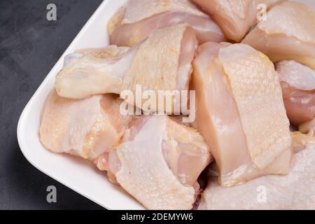 Poulet cru tendre curry coupé avec la peau disposée sur blanc assiette et garniture de poivre noir et de tranches de tomate arrière-plan de couleur graphite Banque D'Images