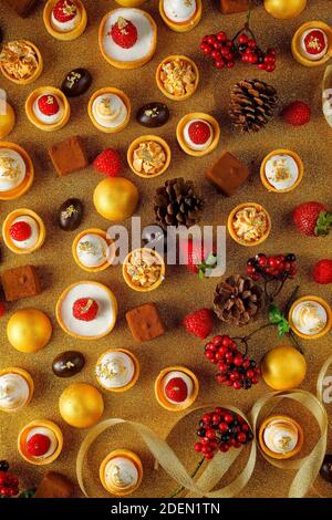 Sélection de délicieux desserts de Noël, petite tarte au citron, chocolats à la truffe, fraises, tartes à la framboise sur fond doré Banque D'Images