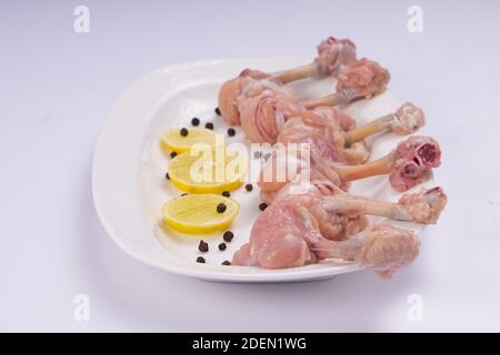 Lipop de poulet cru, six morceaux de lipop de poulet disposés sur une assiette blanche de service avec des tranches de citron et du poivre noir sur fond blanc Banque D'Images