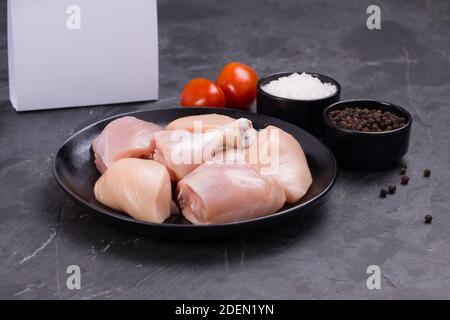 Poulet cru tendre curry coupé sans peau disposé sur noir plaque avec ingrédients de cuisson sur fond blanc avec boîte de livraison à proximité Banque D'Images
