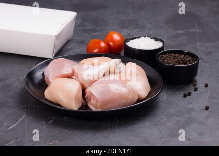 Poulet cru tendre curry coupé sans peau disposé sur noir plaque avec ingrédients de cuisson sur fond blanc avec boîte de livraison à proximité Banque D'Images