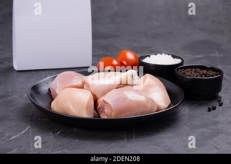 Poulet cru tendre curry coupé sans peau disposé sur noir plaque avec ingrédients de cuisson sur fond blanc avec boîte de livraison à proximité Banque D'Images