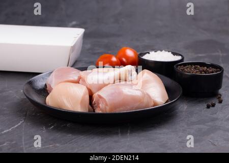 Poulet cru tendre curry coupé sans peau disposé sur noir plaque avec ingrédients de cuisson sur fond blanc avec boîte de livraison à proximité Banque D'Images