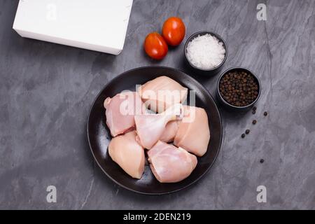 Poulet cru tendre curry coupé sans peau disposé sur noir plaque avec ingrédients de cuisson sur fond blanc avec boîte de livraison à proximité Banque D'Images