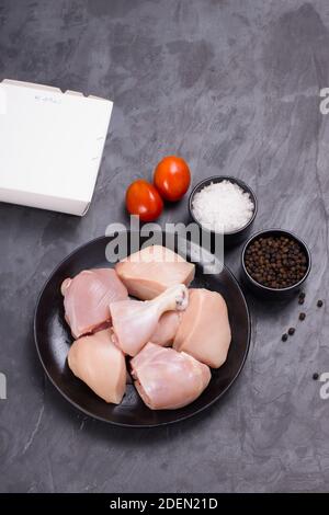 Poulet cru tendre curry coupé sans peau disposé sur noir plaque avec ingrédients de cuisson sur fond blanc avec boîte de livraison à proximité Banque D'Images