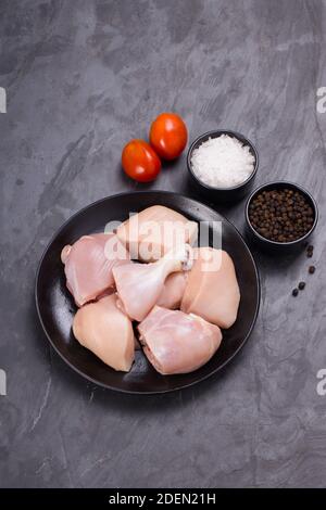 Poulet cru tendre curry coupé sans peau disposé sur noir assiette avec ingrédients de cuisson sur fond blanc Banque D'Images