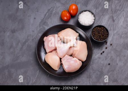 Vue de dessus du poulet cru curry tendre coupé sans peau disposés sur une plaque noire avec des ingrédients de cuisson sur fond blanc Banque D'Images