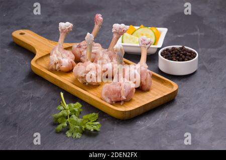 Lollipop de poulet cru, six morceaux de Lollipop de poulet disposés sur un plateau de service avec poivre noir, feuilles de coriandre et tranches de concombre wi en arrière-plan Banque D'Images