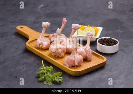 Lollipop de poulet cru, six morceaux de Lollipop de poulet disposés sur un plateau de service avec poivre noir, feuilles de coriandre et tranches de concombre wi en arrière-plan Banque D'Images