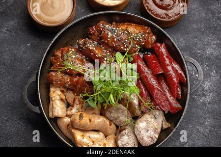 Ensemble de viande pour bière, saucisse, côtes, ailes grillées et trois sauces, sur fond noir Banque D'Images