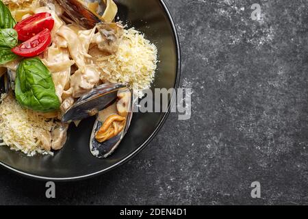 Pâtes avec fruits de mer, moules, pétoncles, rapana et fromage, sur une assiette noire Banque D'Images