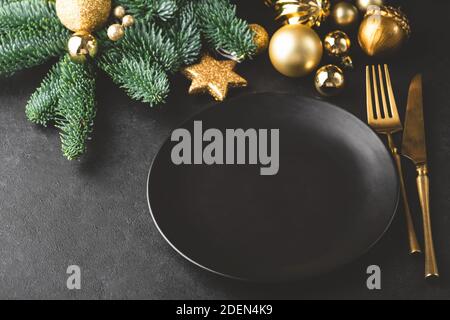 Décor de table élégant de Noël et du nouvel an en noir. Assiette noire, argenterie de couleur dorée, sapin et jouets. Copier l'espace pour le texte, la conception Banque D'Images