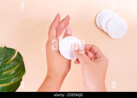 Tampons de coton pour enlever maquillage avec les mains de femme fleurs de coton sur le fond beige, aplatissement Banque D'Images