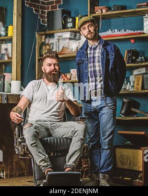 Le client à barbe Hipster s'assoit dans la chaise de salon de coiffure et montre le pouce vers le haut. Le client est satisfait du service dans le salon de coiffure. Hipster avec coupe de cheveux recommande un service de coiffure professionnel, salon sur fond. Banque D'Images