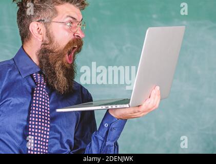 Des informations choquantes. Hipster professeur porter lunettes et cravate tient ordinateur portable surfer sur Internet. Professeur barbu homme choqué avec ordinateur portable moderne surfer sur Internet tableau noir fond. Des nouvelles choquantes. Banque D'Images