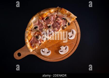 Une vue de dessus d'une pizza fraîche au cheesy avec jambon et champignons sur un plateau en bois Banque D'Images