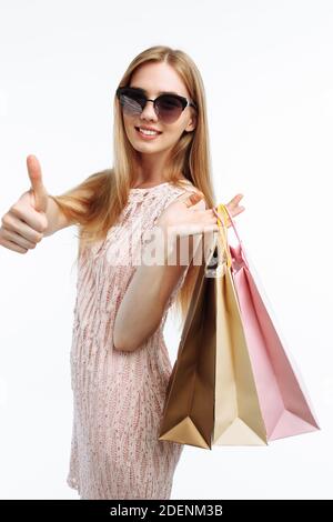 Jeune belle fille posant avec des sacs-cadeaux, se réjouir et montrant le shopping devant l'appareil photo, et montre la classe gestuelle, sur fond blanc, Banque D'Images