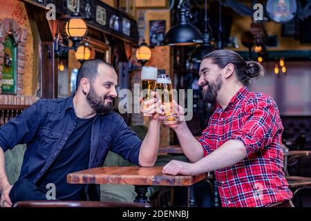 Deux amis de sexe masculin buvant au pub. Ils rient et toastent avec de grands verres pleins de bière. Santé. Banque D'Images