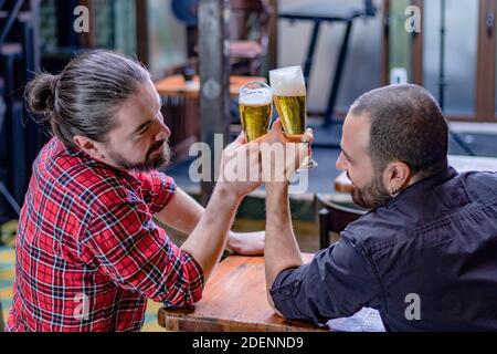 Deux amis de sexe masculin buvant au pub. Ils rient et toastent avec de grands verres pleins de bière. Santé. Banque D'Images