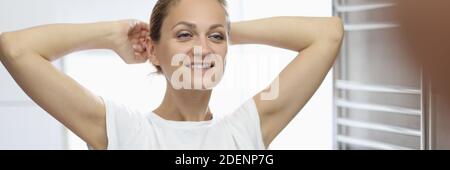 Femme en T-shirt blanc se tient devant le miroir de salle de bains et sourit. Banque D'Images