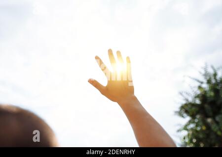 une main atteint pour le ciel et couvre le soleil, les rayons du soleil font leur chemin à travers la main, gros - vers le haut Banque D'Images