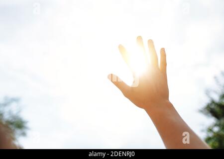 une main atteint pour le ciel et couvre le soleil, les rayons du soleil font leur chemin à travers la main, gros - vers le haut Banque D'Images