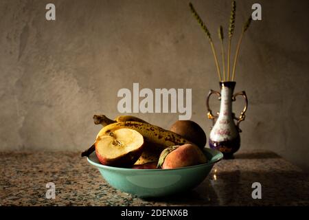 La vie de fruit assis dans une assiette avec des oreilles de blé dans un pot brouillant dans le fond. Ambiance rustique avec lumières tamisées et tons dorés Banque D'Images