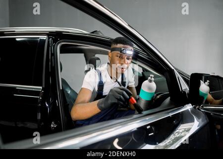 Vue de face de l'homme africain de beau atelier de détail de voiture, essuyant porte de voiture panneau en cuir avec brosse douce et anti professionnel spécial Banque D'Images