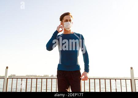 Beau mâle caucasien dans les vêtements de sport pose sur la plage portant un masque. Banque D'Images