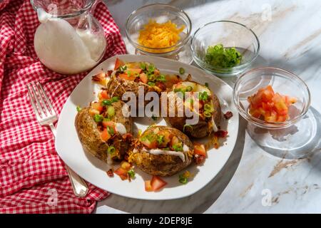 Pommes de terre cuites au four avec fromage cheddar, morceaux de bacon émiettés, échalotes tomates en dés et sauce ranch Banque D'Images